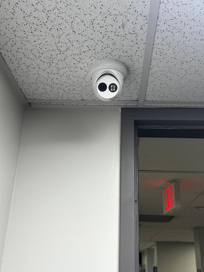 White turret security camera installed on an office ceiling above a doorway